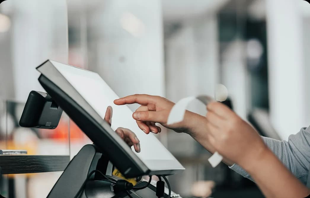 A hand tapping a countertop point-of-sale terminal as a receipt prints
